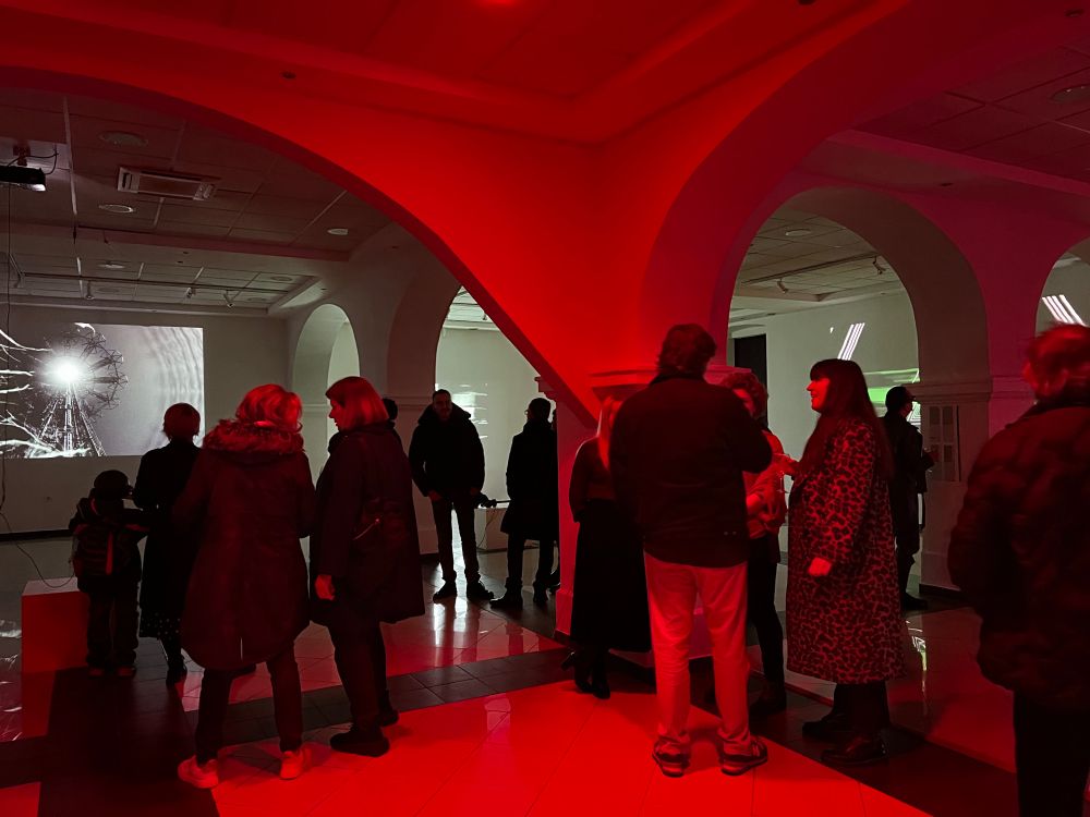 Crowd at the opening of the exhibition T.F.I.D. (The Future is Dead). On the main screen an Embryoroom video is playing, depicting a nightmarish version of the Coney Island Tower. The entire space is lit in red. 