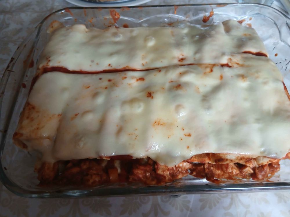 Photo of a glass dish filled with oven-baked cheese-topped enchiladas