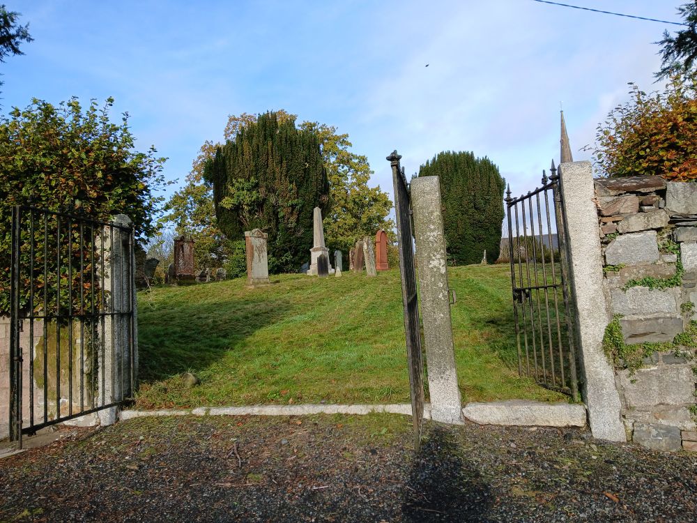 Entrance to an old churchyard with three metal gates standing open. 