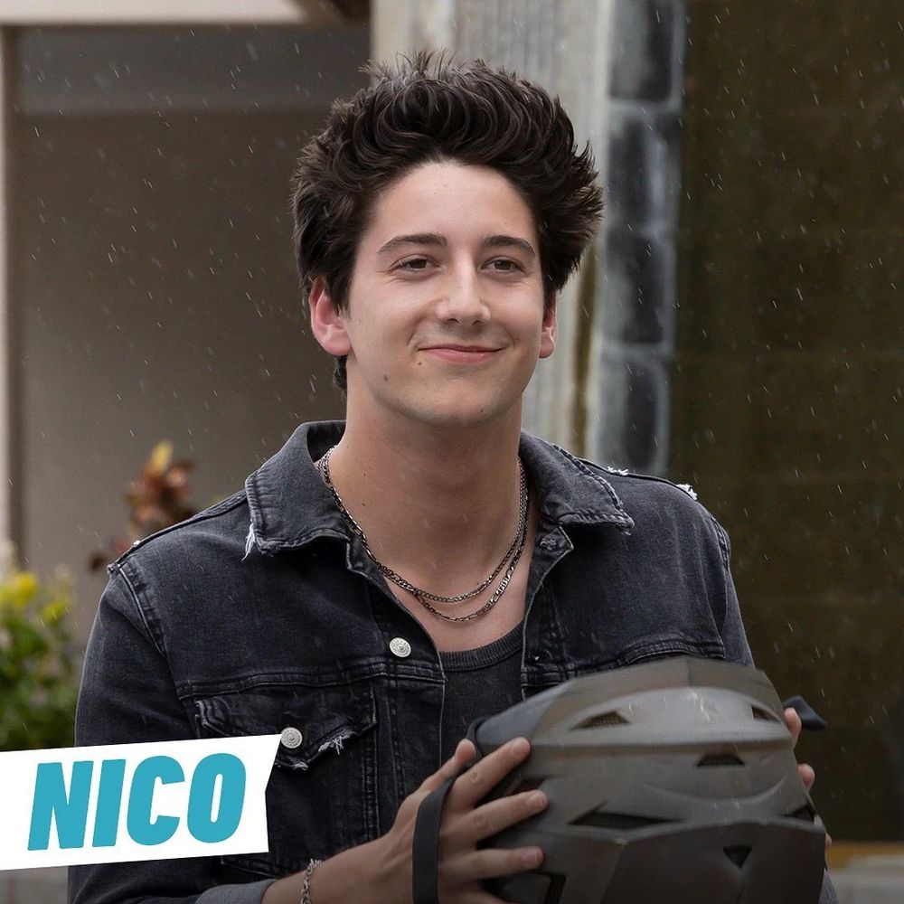 Nico, un chico de piel clara y pelo oscuro vestido de negro y con cadenas al cuello y un casco de moto
