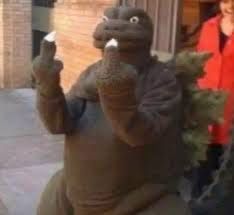 A cheap looking Godzilla holding up two middle fingers.