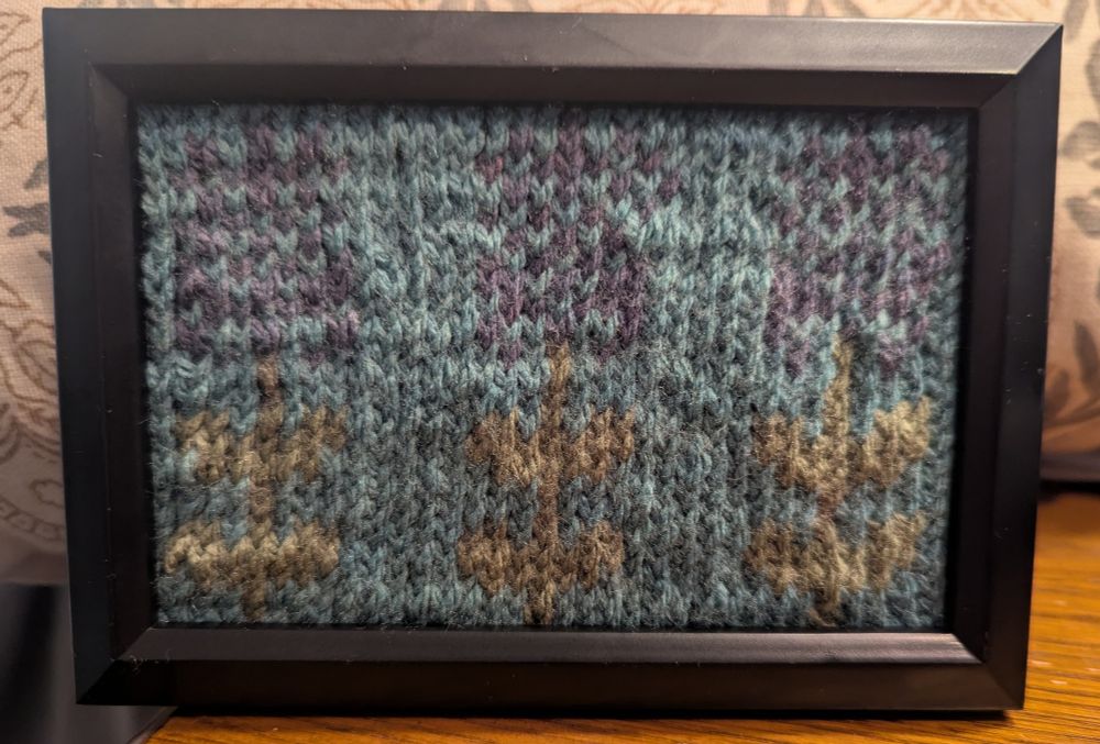 Framed knit artwork with lavender motif against blue background