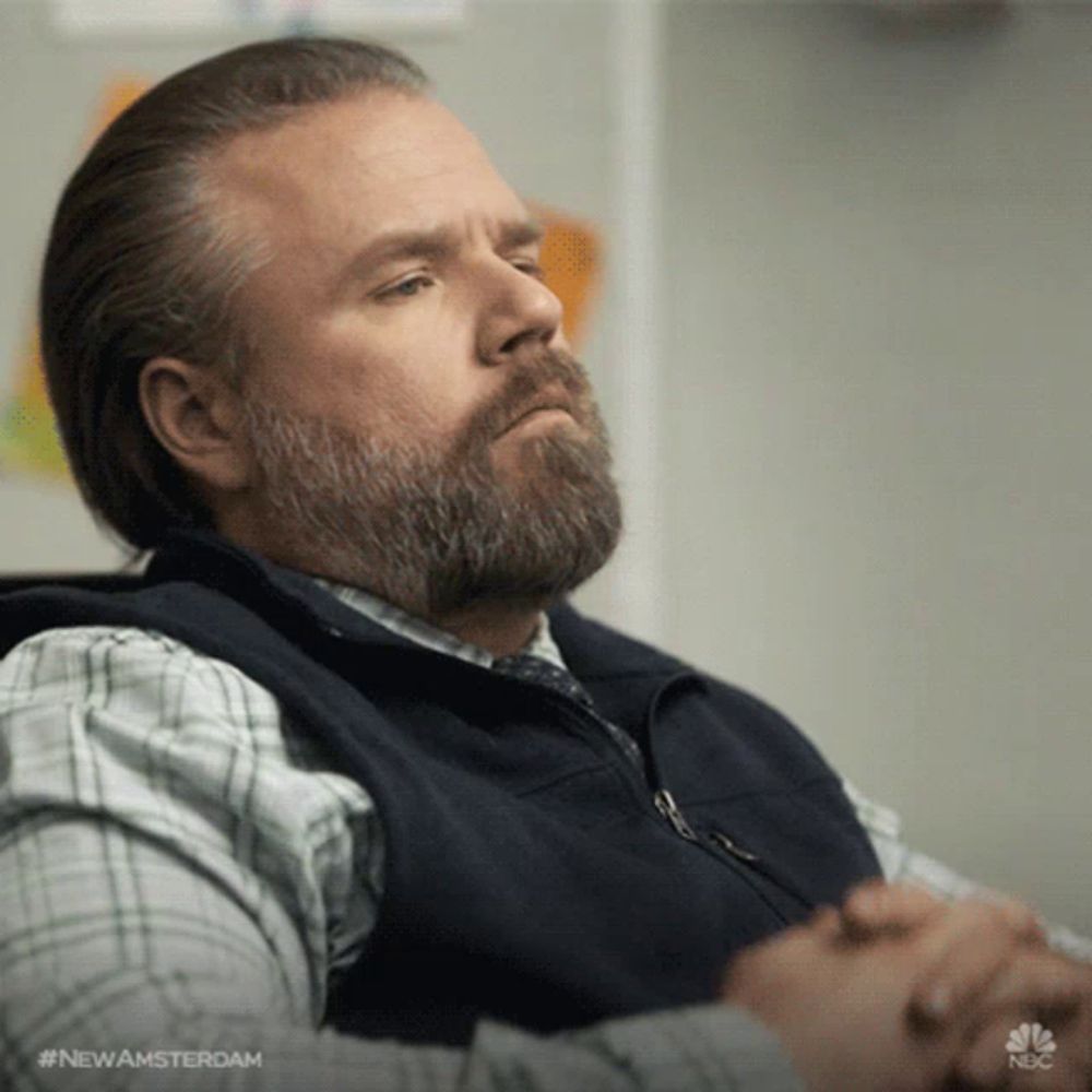 a man with a beard is sitting in a chair with his hands folded in front of him