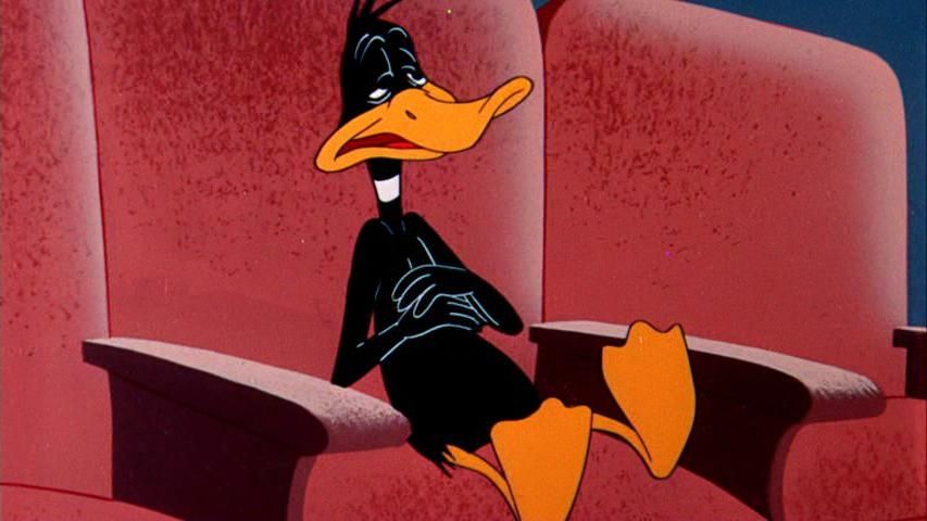 Daffy Duck sitting in a seat in a theater, eyes nearly shut, a sour expression, clearly nauseous. Still image from "This Is a Life?" (1955)
