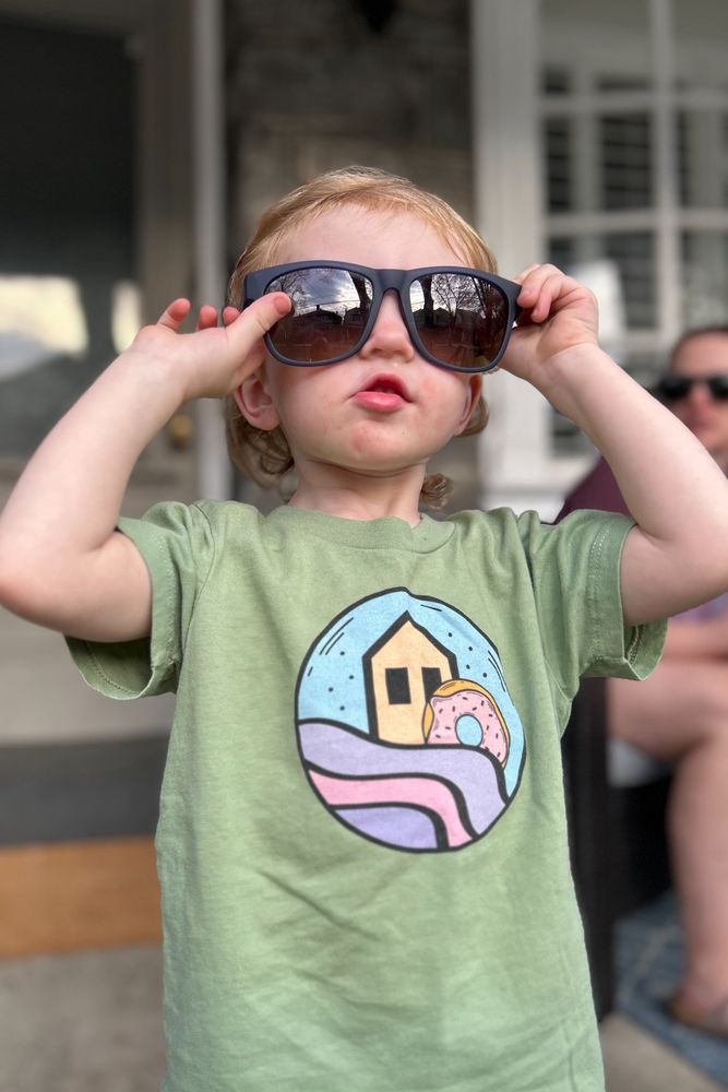 A toddler wearing adult sunglasses and a waterwheel t shirt 
