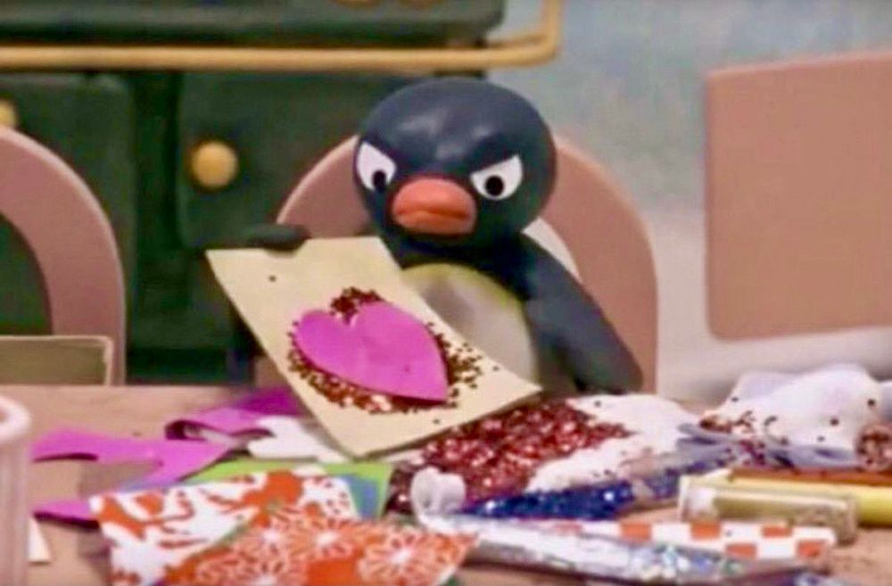 An angry Pingu The penguin staring at a piece of paper with a heart and poorly applied glitter that he made. His table is a mess, even if he is creatively free 