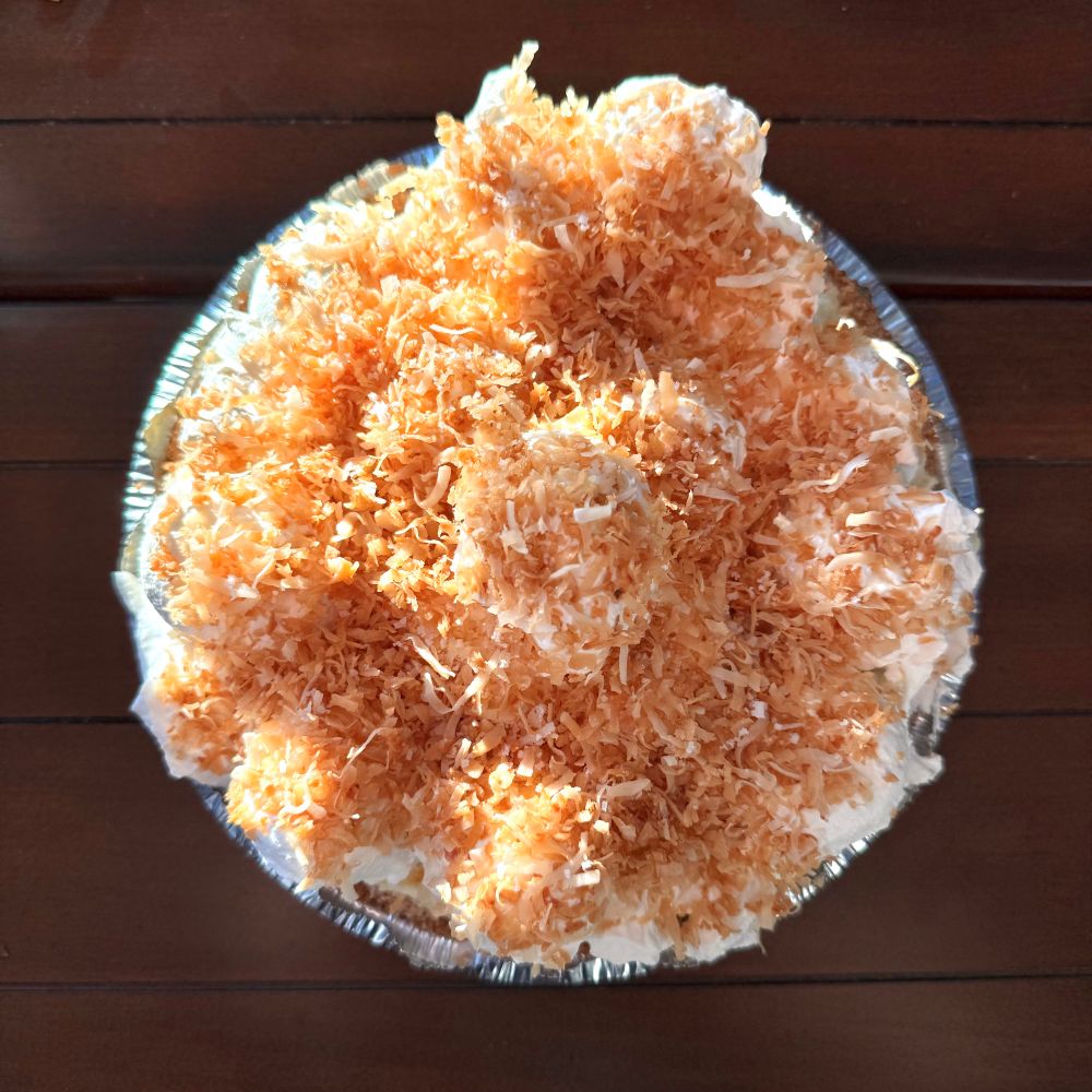 A photo of a coconut cream pie heaped with whipped cream and abundant toasted coconut 