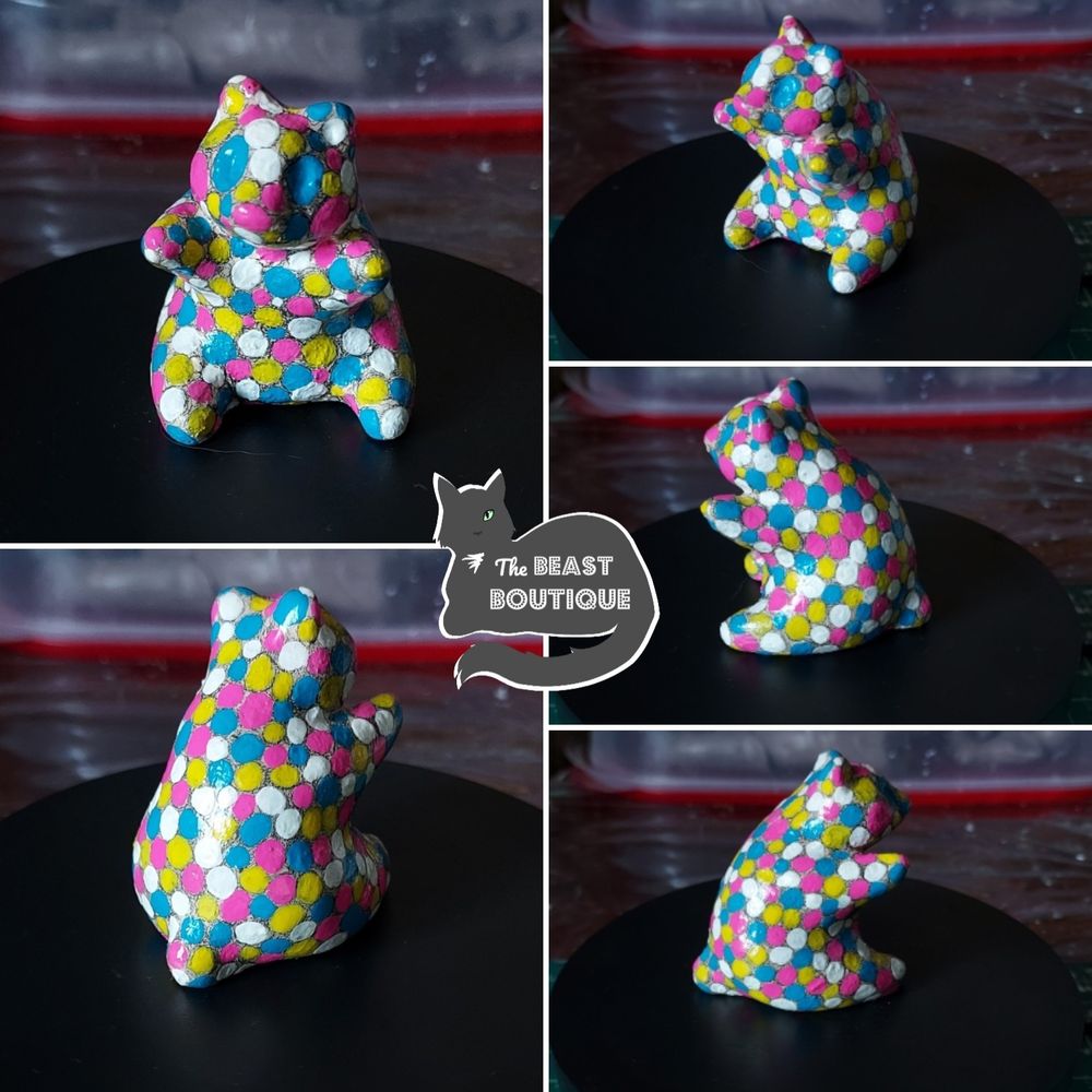 a collage showing a sitting panda figurine from multiple angles. the panda is covered in large white, blue, pink, and yellow polka dots, all nearly touching, with negative space in a pale orange visible between them. 

the image is watermarked with a logo of a one-eyed grey cat, and the words 'the beast boutique.'