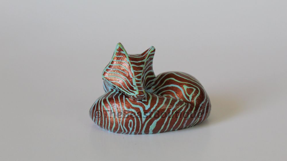 a metallic copper sleeping fox figurine with blue and green lines, like ripples in water, drawn all over its body. 

the shop name, the beast boutique, watermarks the image. 