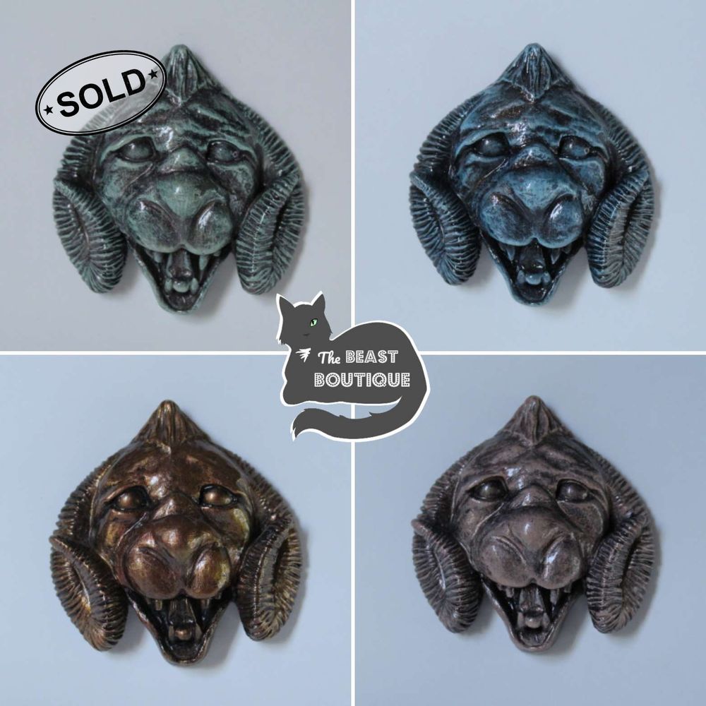 a collage of four lion-faced gargoyle magnets, with curling ram horns on the sides of their heads. Clockwise from the top, they are painted in  green, blue, pink faux patina styles. The last magnet is painted bronze. The green magnet has a sold stamp on it. 

the shop name, the beast boutique, watermarks the image. 