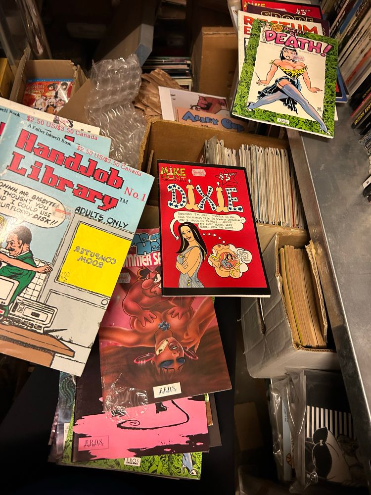 verschiedene bunte US Porno-Comics aus den 90er Jahren zwischen überfüllten Kisten und Regalbrettern