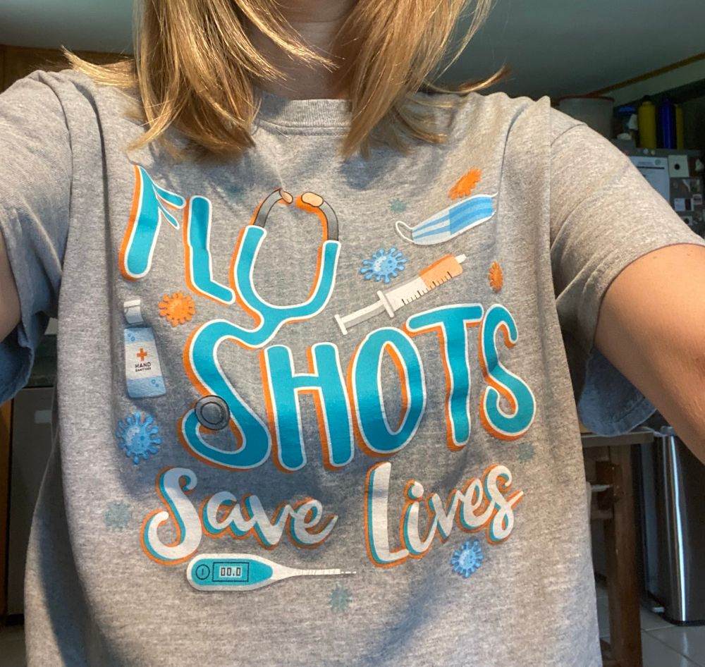 Me wearing a t-shirt with pictures of a thermometer, germs, masks, pill bottles, and a syringe with the words “Flu shots save lives.”