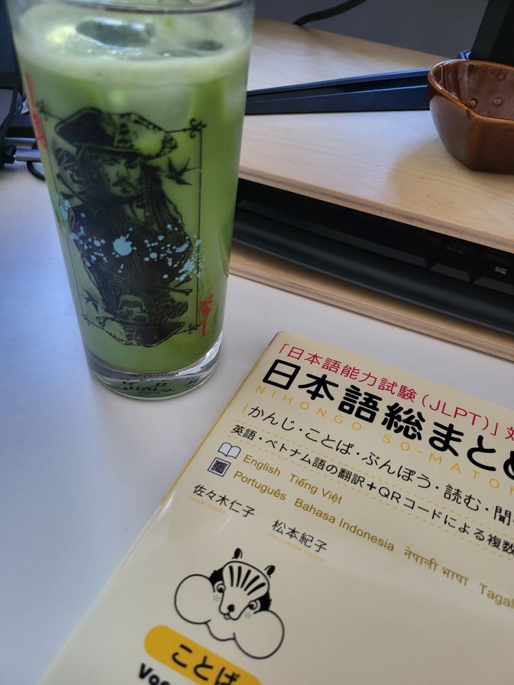 Matcha-Latte in einem hohen Glas und ein japanisch Lehrbuch auf dem Tisch