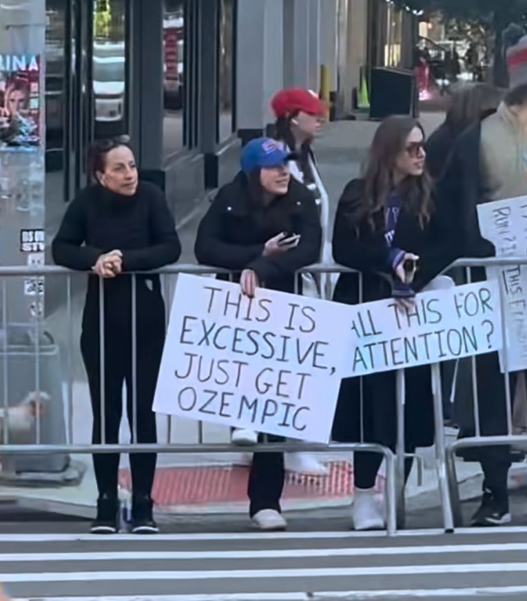 A lady with a sign that says “this is excessive, just get ozempic”