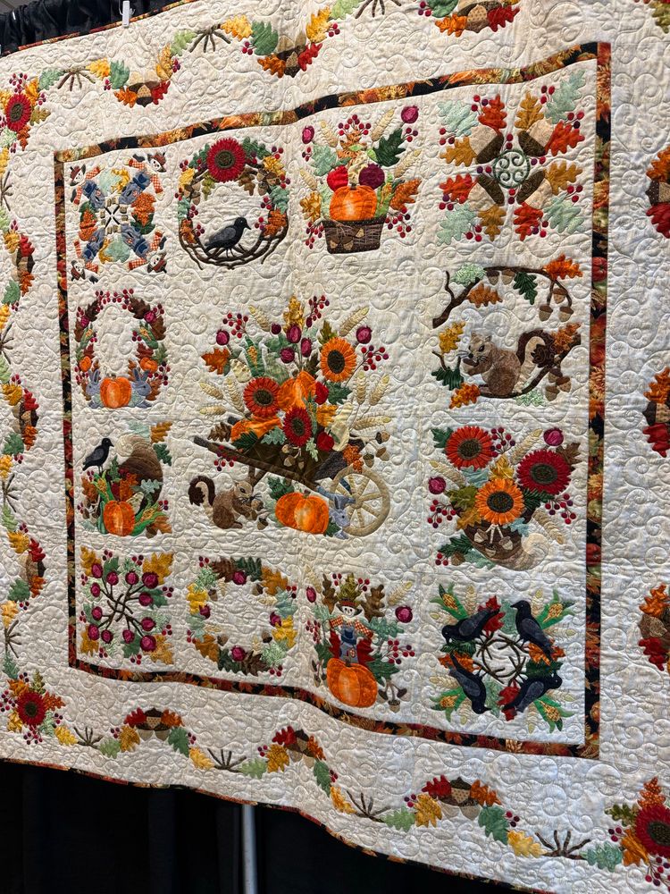 A white quilt with fall themed flowers and gourds and woodland creatures all over it