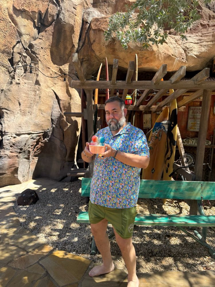 old white guy in a floral shirt with a rainbow mickey mouse ear shaved ice in his hands