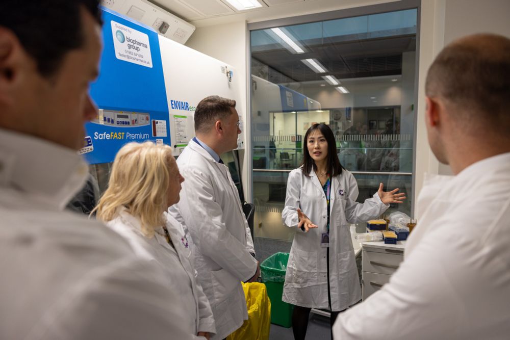 A scientist in a Cancer Research UK lab coat speaks to a group of visitors to a laboratory