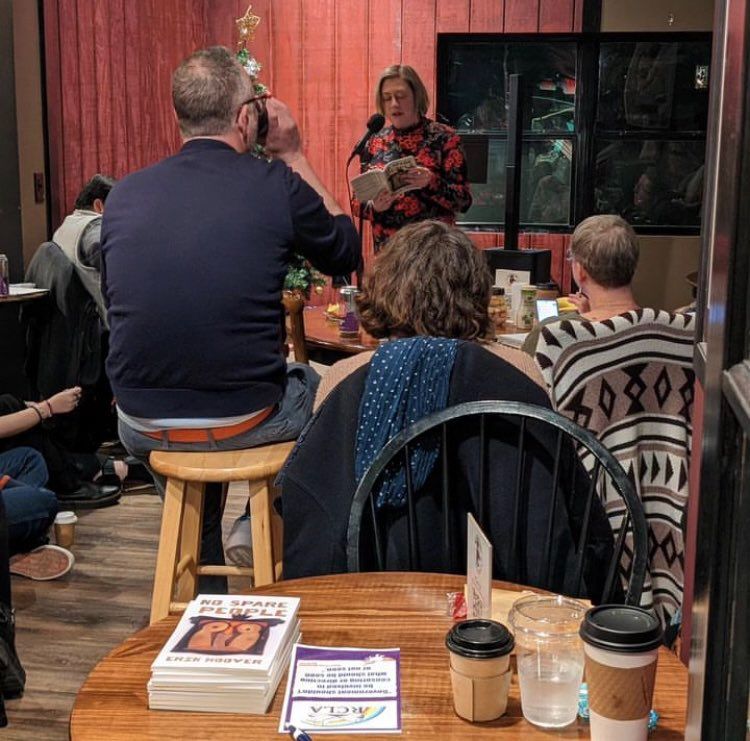 Erin Hoover reading in the background; copies of No Spare People on a table in the foreground