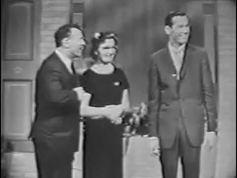 Host Johnny Carson onstage with two contestants, presumably husband and wife, in an episode of Do You Trust Your Wife?