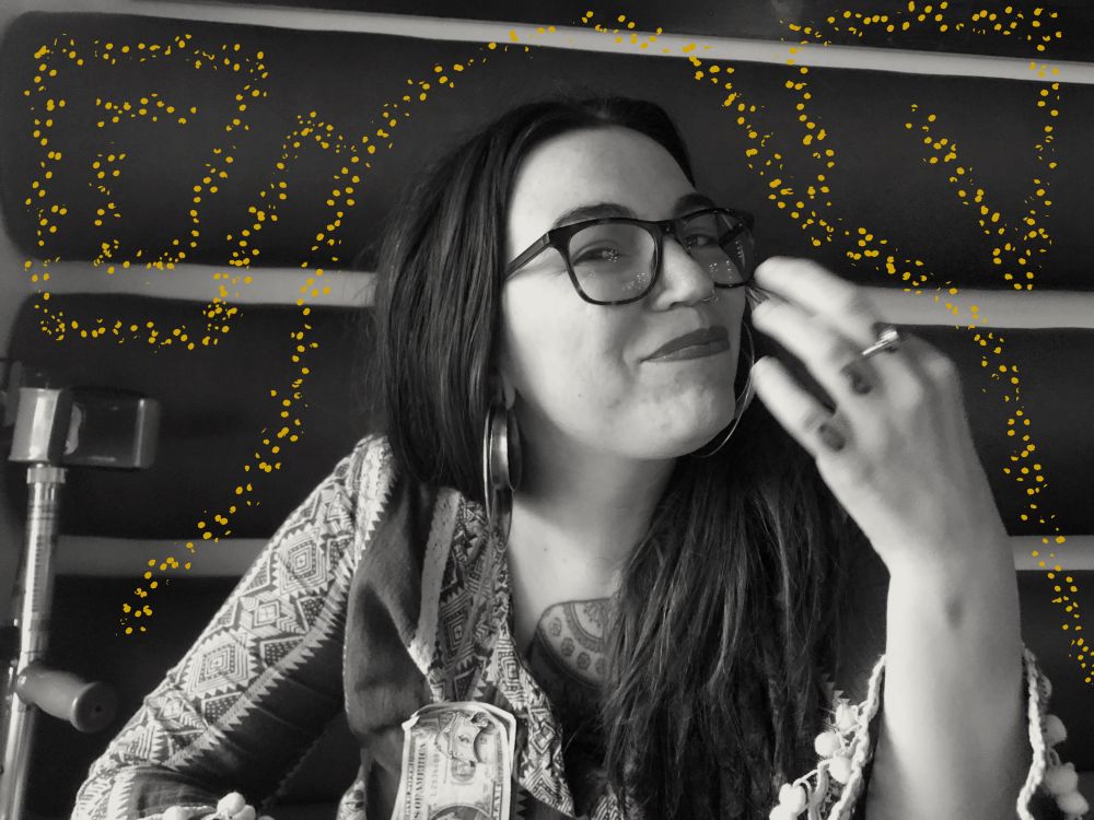 Black and white photo of Destiny with a closed mouth smile looking at the camera. A forearm crutch is in view, leaning against the striped wall in the background. A dotted, Taino inspired geometric illustration fills the negative space.