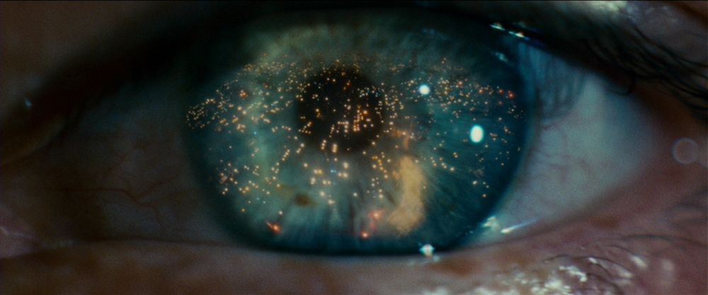 Close-up of an eye with blue iris reflecting the lights of a futuristic city.