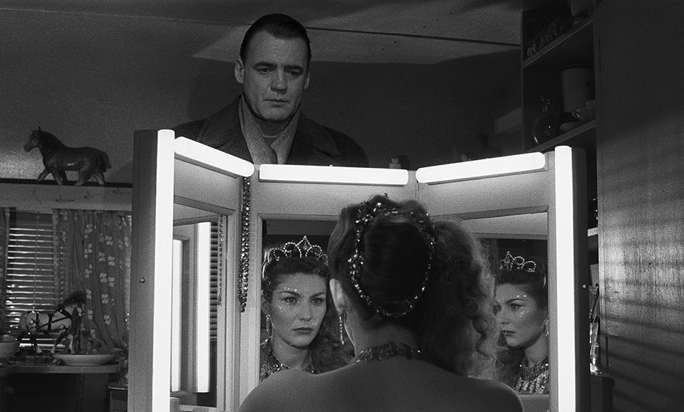 The picture shows Marion seated at a brightly lit vanity mirror. She is dressed in an elegant outfit with a tiara, and her face is reflected multiple times in the mirror's panels, adding depth to the image. Behind the mirror, Damiel is visible, observing her silently with a calm, contemplative expression. The room is intimate, featuring small details like a horse figurine on a shelf, patterned curtains, and various personal items, creating a warm yet reflective atmosphere.

Have a great day! <3