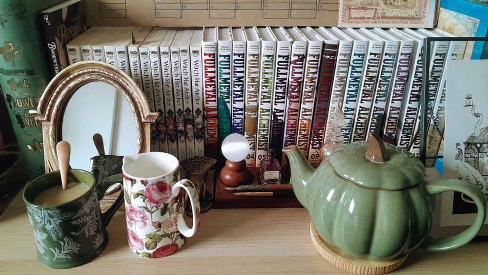 Green pumpkin-shaped teapot, patterned mug and pot, along with mirror, inking set and comic books in the background.