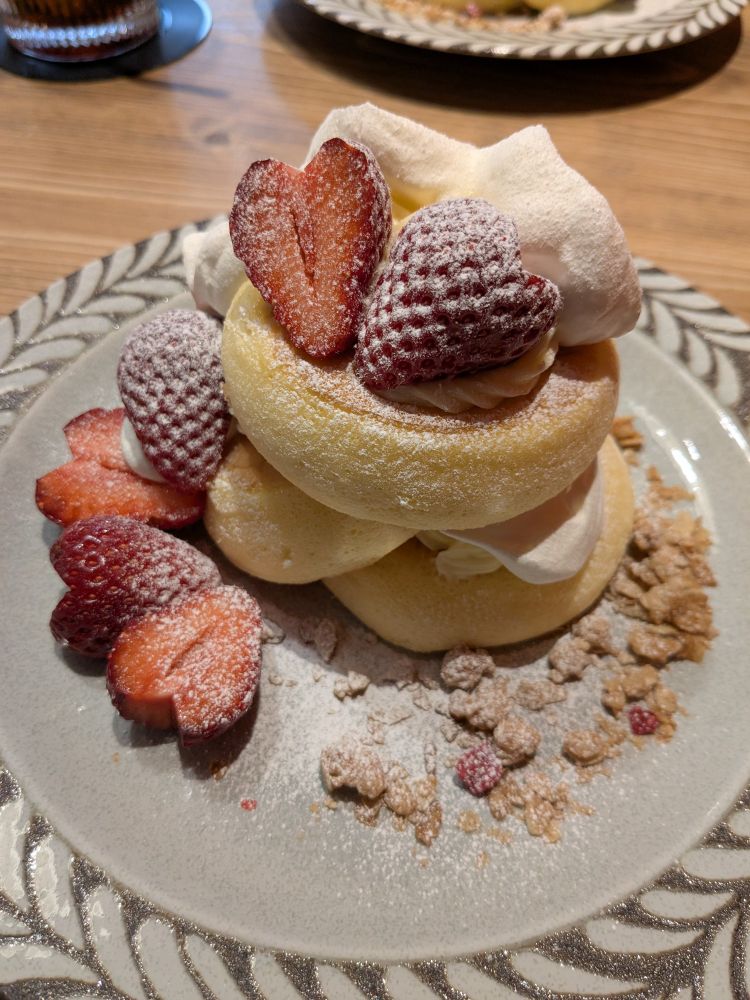 ハート型に切られた苺と生クリーム、カスタードクリームが乗ったスフレパンケーキ。粉砂糖とコーンフレークがまぶしてある。