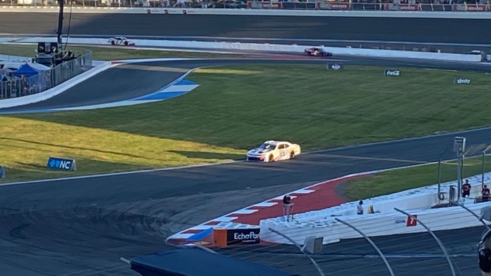 Connor Zilisch’s white #88 Chevy is highlighted by a beam of sunlight breaking through the stands as he approaches turn 7 at the Charlotte Roval.