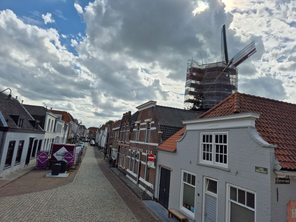 Uitzicht op een ingepakte molen, een bouwbak met hekken, een brengparkje en een schattig oud straatje. 
