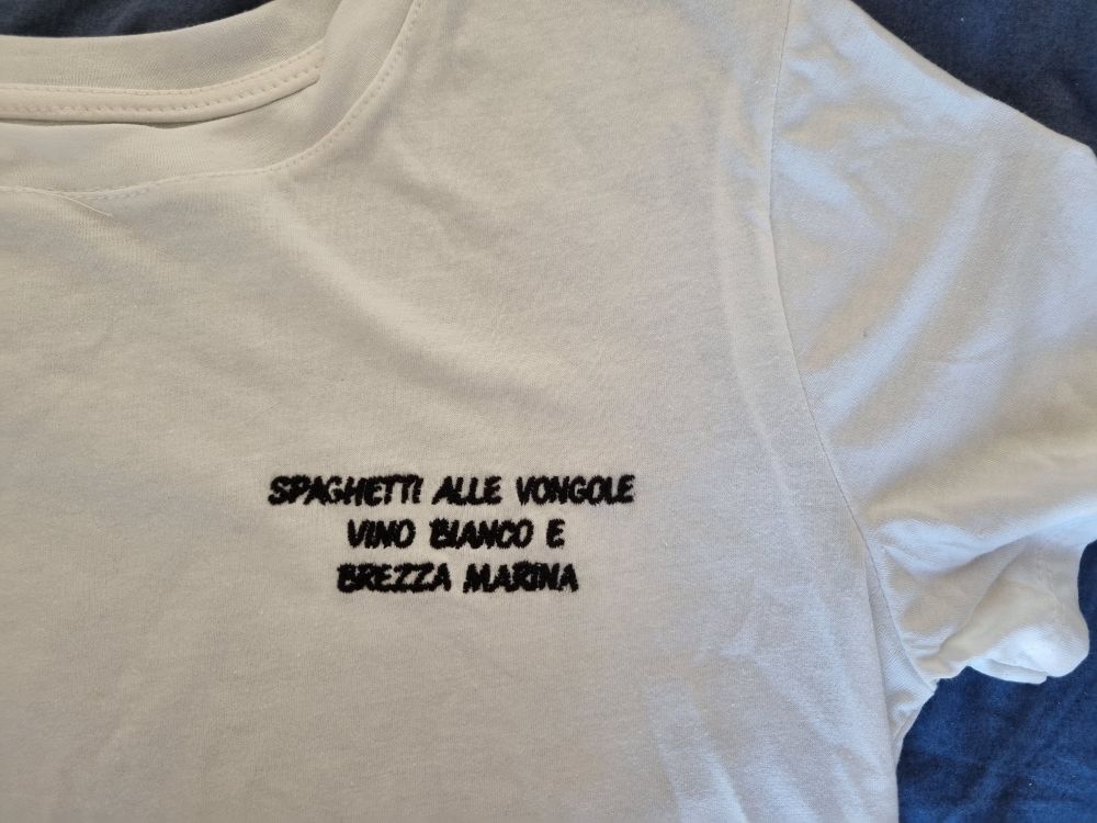 Weißes Shirt bestickt in schwarz mit der Aufschrift 
SPAGHETTI ALLE VONGOLE
VINO BIANCO E
BREZZA MARINA