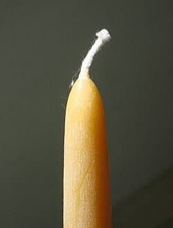The top of a tapered yellow-but-also-weirdly-flesh-toned candle with a white wick jutting out and angled to the right
