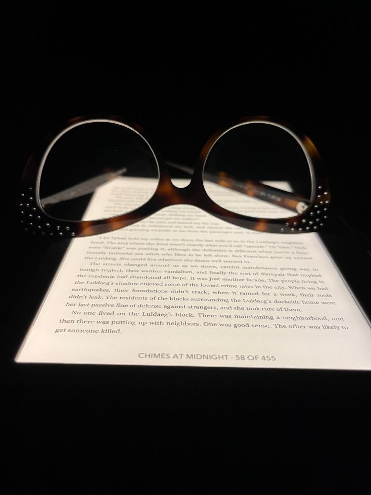 a pair of glasses atop the glowing screen of an ereader. the footer reads, 
Chimes at Midnight • 58 of 455
all else is dark.