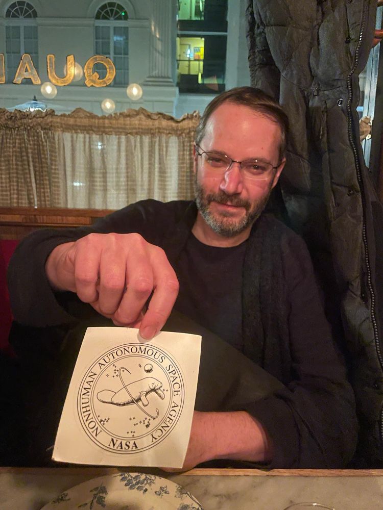 A very handsome man named Fred in a black sweater shows you a Nonhuman Autonomous Space Agency sticker