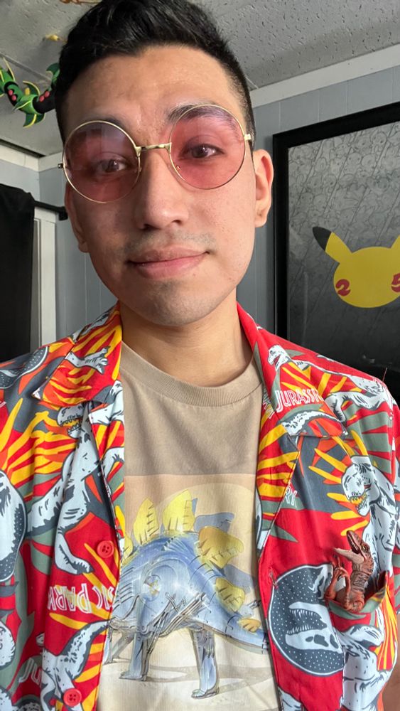 Selfie wearing Jurassic clothing with a velociraptor figure in the chest pocket and wearing sunglasses 