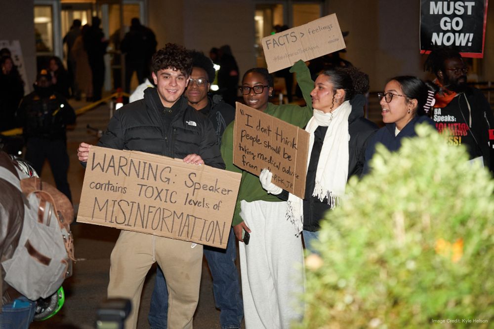 Group of students holding signs, visible sign reads: "Warning, Speaker contains toxic levels of misinformation" 