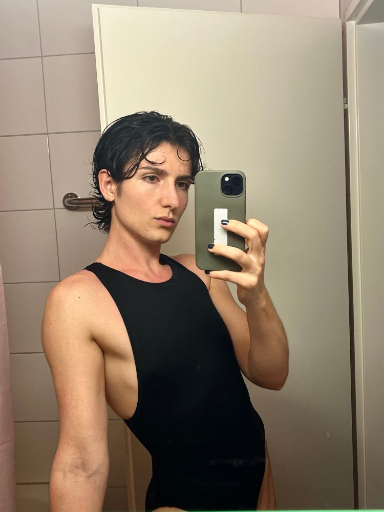 hot androgynous person standing in front of a mirror wearing sporty black swimming suit, short wet hair and nail polish 