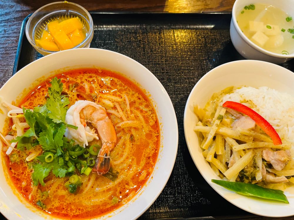 お盆にトムヤムヌードル、グリーンカレー、オレンジ色のゼリー、豆腐スープが載っている。