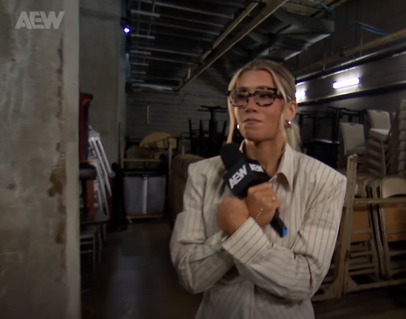 Lexi Nair on AEW Collision wearing some large spectacles and a pinstripe blouse.