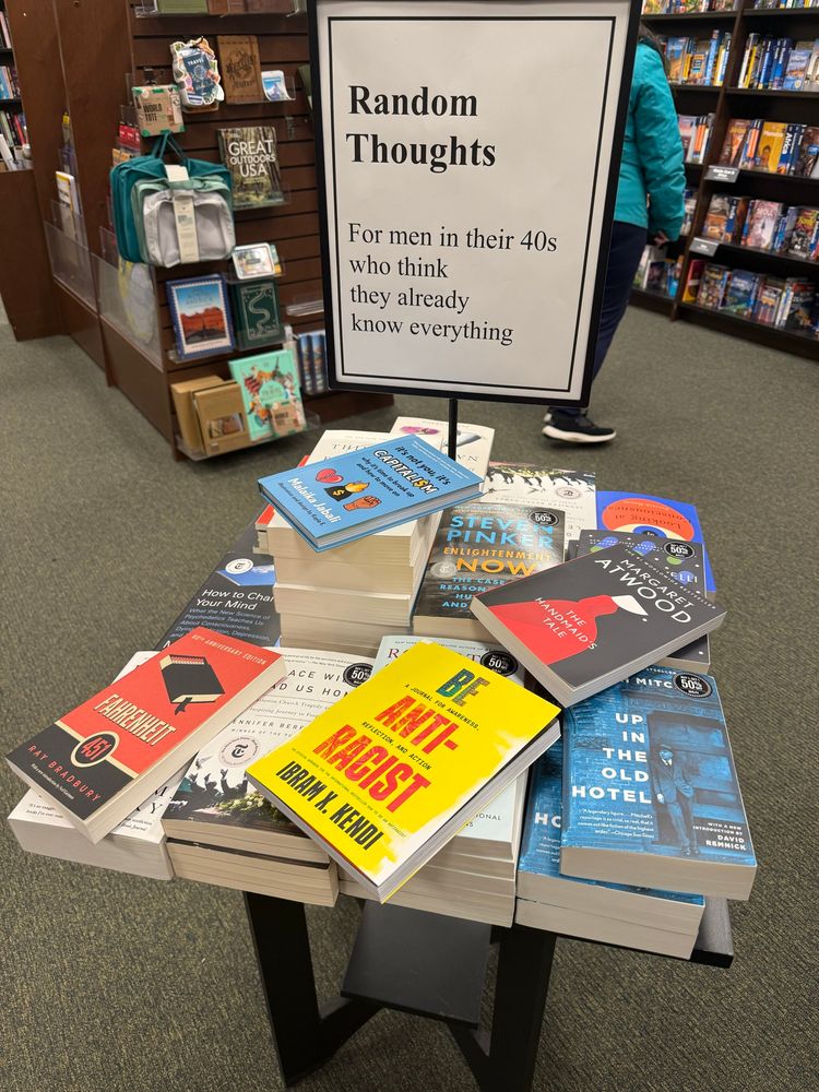 Image of a bookstore display shelf labeled “Random thoughts for 40 year old men who think they already know every thing” and four books have been added to the collection: “Be Anti-Racist”, “The Handmaid’s Tale”, “Fahrenheit 451”, and “it’s not me, it’s capitalism”