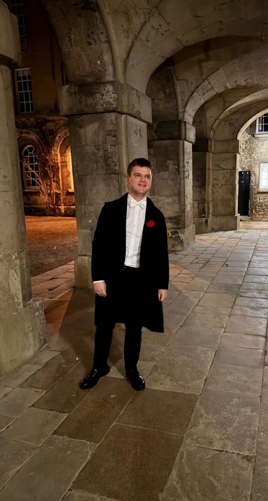 Morten in formal Oxford examination academic dress, looking pensive, contemplating his next career move now that he has his Phd, surrounded by majestic columns in Oxford