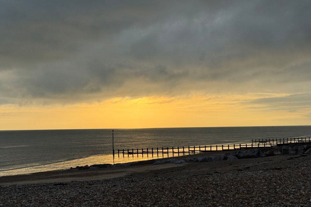 Golden light breaks through dark grey skies over the shingle beach 