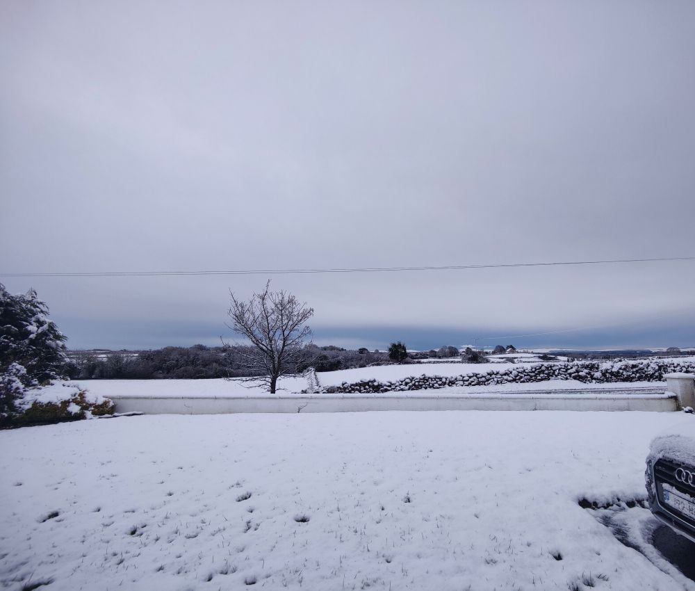 Photograph of a snowy garden scene with stone walls and mountains in the background.