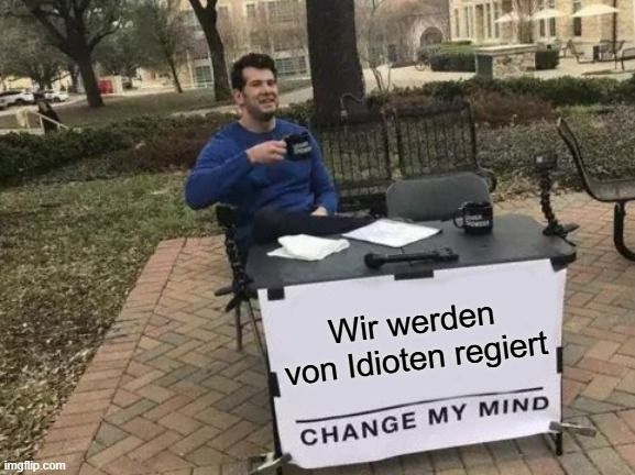 Mann am Tisch mit Schild mit Aufschrift "Wir werden von Idioten regiert"
