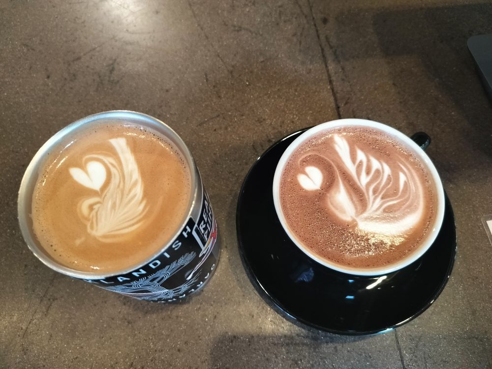 Two cafe drinks with fancier than usual foam art (feathery leaf/wing curled around a small heart)