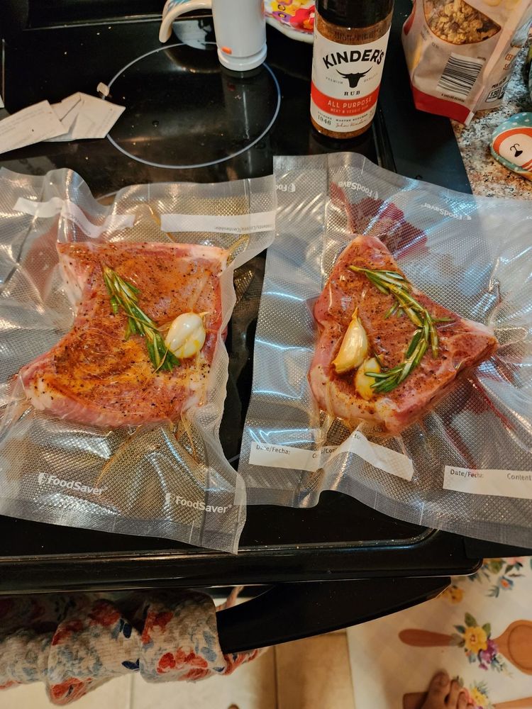 Two vacuum sealed frozen pork chops, spice rubbed and sealed with fresh garlic and rosemary