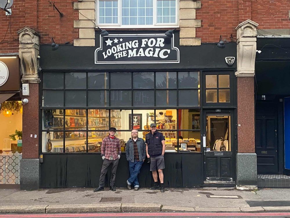 sign above record shop with three gentlemen stood below.
