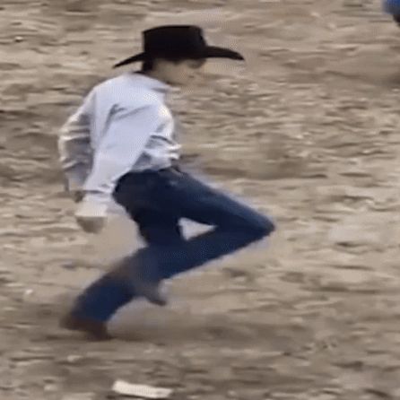 a man in a cowboy hat is walking on a dirt path