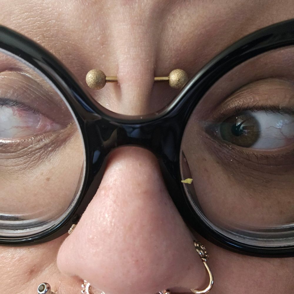 close-up of a face wearing glasses and with multiple facial piercings 
