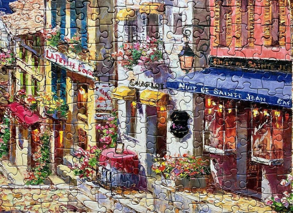 A close up view of Archway to Cagne jigsaw puzzle from Cobble Hill showing off the little boutique shops that are built from stone and have a European feel.  There are floral baskets hanging from the upstairs windows and a cobble stone street. 